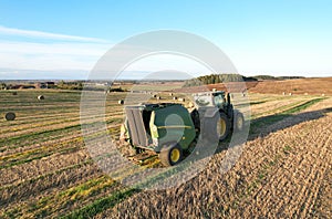 John Deere Tractor 6715R with John Deere V461R round baler making Hay Bales in an agricultural field. Farm Round Hay Bale Tractor