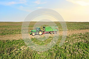 John Deere Tractor with trailer working in a potato field. Agricultural tractor at field. Seasonal harvesting of potatoes from the