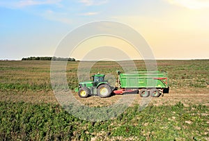 John Deere Tractor with trailer working in a potato field. Agricultural tractor at field. Seasonal harvesting of potatoes from the