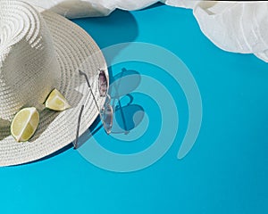 John Lennon style sunglasses. White hat and a piece of fabric all ready for the beach. Blue background. Concept set