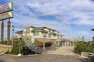 Johnnie Mercer's Fishing Pier with a brown wooden pier, light posts, green plants, brown sand, blue sky and clouds