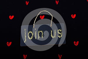 Join us label on a black notice board and red hearts