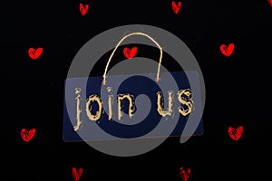 Join us label on a black notice board  and red hearts