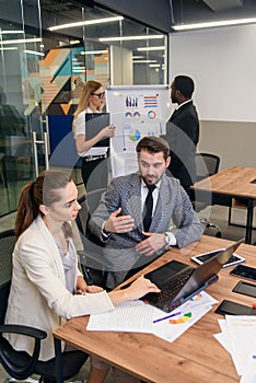 Joined work of two confident business people in formal suit working together with laptop at office with their coworkers