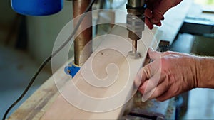 joiner is drilling wood detail, making hole in wooden board by drill in workshop