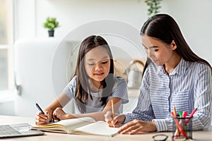 Joint activities and interests concept. Young asian mother and daughter drawing with markers, sitting in kitchen