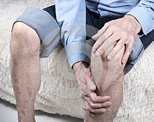 Joint disease, arthritis or arthrosis. Elderly man sitting on sofa and suffering from pain in knee