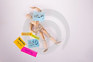 Jointed Wooden doll laying down holding a help picket sign sticky notes SEO ranking websites keywords