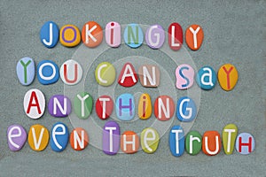 Jokingly you can say anything even the truth, creative quote composed with multi colored stone letters over green sand