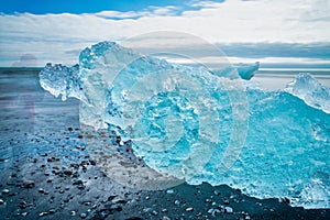 Jokulsarlon Diamond Beach with photographer moving close to iceberg on a sunny day, Iceland. Long exposure view