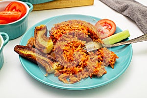 Jollof rice with fried banana on a plate. Rice with tomatoes, onions, spices. Fresh vegetables. White background