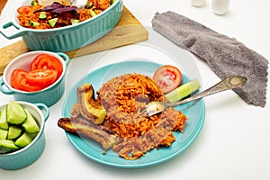 Jollof rice with fried banana on a plate. Rice with tomatoes, onions, spices. Fresh vegetables. White background