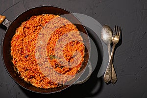 Jollof rice in a frying pan on a dark background. A traditional Nigerian dish of rice, tomatoes and spices