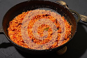 Jollof rice in a frying pan on a dark background. A traditional Nigerian dish of rice, tomatoes and spices