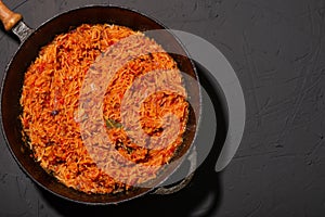 Jollof rice in a frying pan on a dark background. A traditional Nigerian dish of rice, tomatoes and spices
