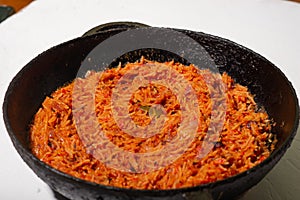 Jollof rice in a frying pan on a white background. A traditional Nigerian dish of rice, tomatoes and spices