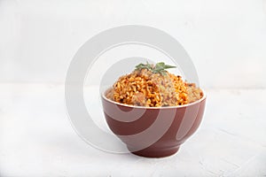 Jollof rice with parsley in a ceramic cup on a white background. National cuisine of Africa. Copy spaes