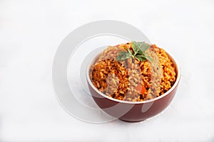 Jollof rice with parsley in a ceramic cup on a white background. National cuisine of Africa. Copy spaes