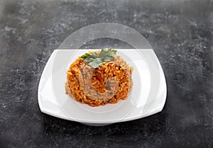 Jollof rice with parsley on a plate on a black background. National cuisine of Africa