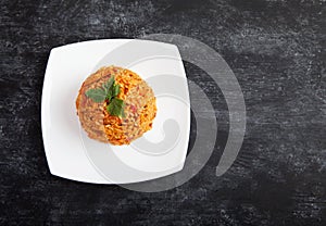 Jollof rice with parsley on a plate on a black background. National cuisine of Africa