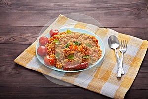 Jollof rice, tomatoes and hot peppers on a blue plate, fork, spoon on a linen napkin on a brown wooden background. National