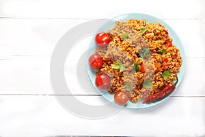 Jollof rice, tomatoes and hot peppers on a blue plate on a white background. National cuisine of Africa