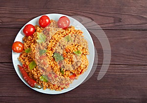 Jollof rice, tomatoes and hot peppers on a blue plate on a wooden background. National cuisine of Africa