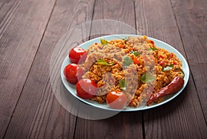 Jollof rice, tomatoes and hot peppers on a blue plate on a wooden background. National cuisine of Africa