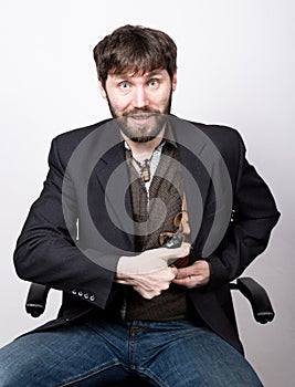 Jolly bearded man in a jacket and jeans, sitting on a chair and holding a gun. gangster concept