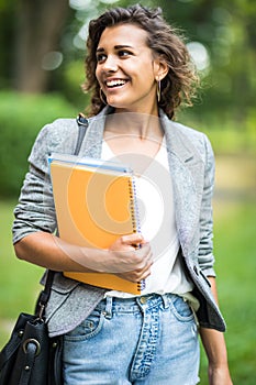 Jolly carefree girl embracing books in park while coming home after classes in university. Cheerful attractive young woman looking