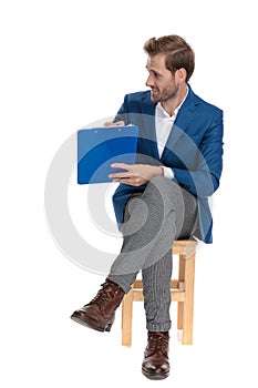 Jolly casual man presenting his clipboard while sitting