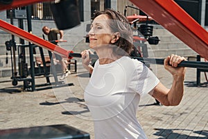 Jolly elderly female enjoying workout on sports ground