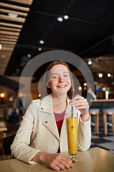 Jolly student girl drinking juice in cafe