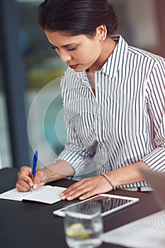 Jotting down her ideas. a young businesswoman writing notes at an office desk.