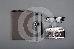 Journalist or blogger table - spiral blank notebook, pencil, camera and glasses on gray background, top view