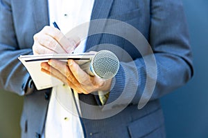 Journalist, correspondent or reporter at media event, holding microphone, writing notes.