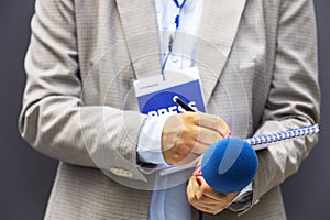 Journalist correspondent or reporter with press pass at media event, holding microphone, writing notes. Journalism concept