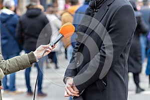 Journalist holding microphone making media interview with male politician or business person. Street interview or vox popoli.