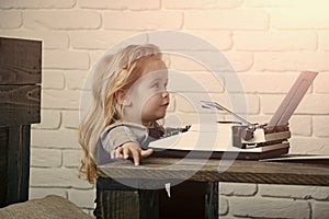 Journalist kid sitting at table and typing typewriter with paper
