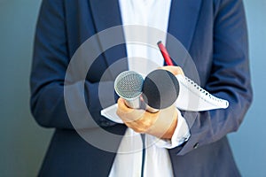 Journalist at media event or news conference, holding microphone, writing notes. Broadcast journalism concept.