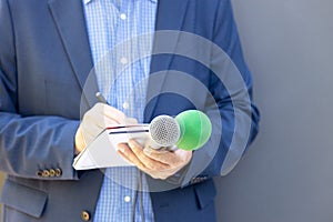 Journalist at media event or press conference, holding microphone, writing notes. Broadcast journalism concept