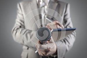 Journalist at a news press conference or media event holding a microphone and writing notes