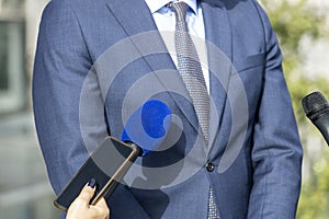 Journalist at press conference or news event holding microphone and smartphone making media interview with business person