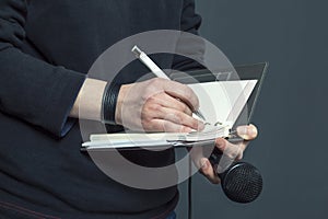 Journalist at press conference, writing notes, holding microphone.