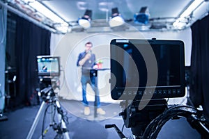 Journalist in a television studio is talking into a microphone, blurry film cameras