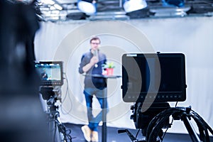 Journalist in a television studio is talking into a microphone, blurry film cameras