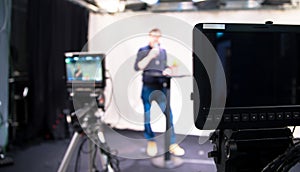 Journalist in a television studio is talking into a microphone, blurry film cameras