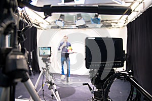 Journalist in a television studio is talking into a microphone, blurry film cameras