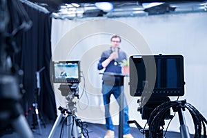 Journalist in a television studio is talking into a microphone, blurry film cameras