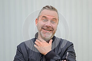 Jovial man laughing at the camera raising his hand to his throat